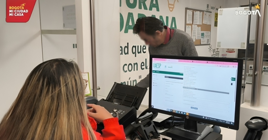 Foto que muestra dos personas hablando y un computador 