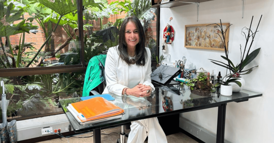Tania Rodríguez dentro de una oficina rodeada de plantas ornamentales y vegetación visible a través de un ventanal en el Jardín Botánico de Bogotá.