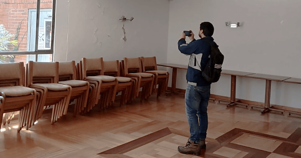 Personal del IDIGER realiza visita técnica para inspeccionar salón con daños visibles en pared, sillas apiladas y mesas laterales en unidad residencial de Bogotá.