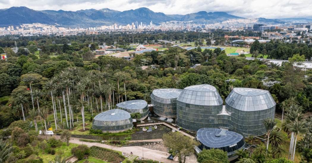 Vista panorámica del Jardín Botánico de Bogotá con Tropicario, zonas verdes y viviendas y edificaciones al fondo
