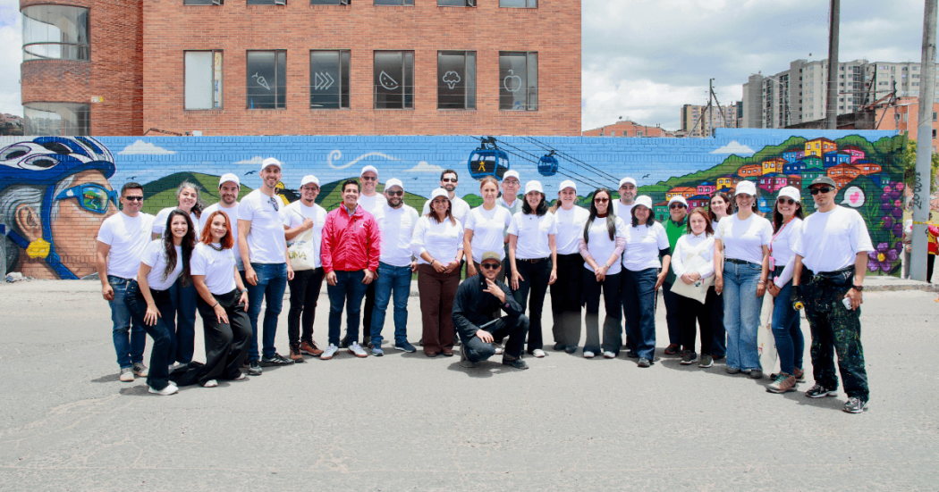 Grupo de personas posa frente a un mural colorido en Ciudad Bolívar, durante el lanzamiento de la segunda Zona Urbana por un Mejor Aire de Bogotá.