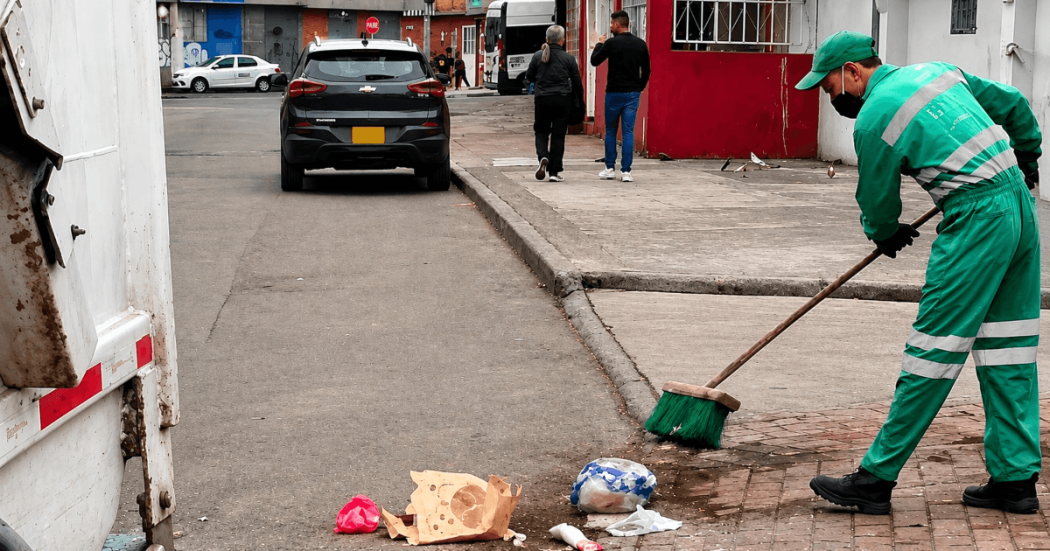 Foto que muestra una persona barriendo la calle y un camion recolector