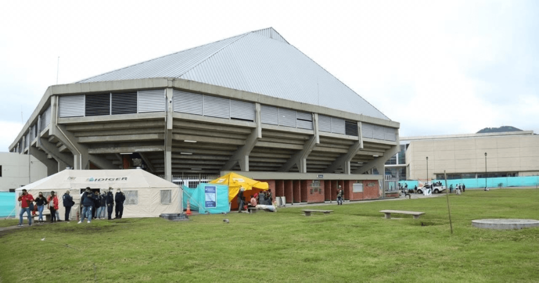 Vista exterior del Palacio de los Deportes en Bogotá con carpas institucionales, personas y un punto de recepción de ayudas humanitarias instalado sobre una zona verde.