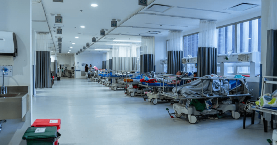 Foto que muestra la sala de urgencias de un hospital, con varios pacientes recibiendo atención en las camillas de la sala.