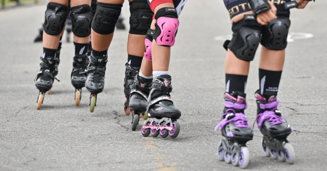 Primer plano de varias personas practicando patinaje sobre una vía, con patines en línea, cascos y elementos de protección.
