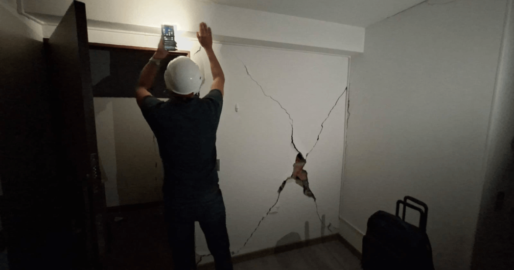 Foto que muestra una persona con un casco revisando una pared con una grieta