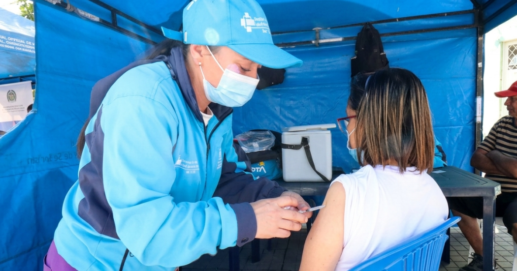 Foto que muestra a una persona del equipo de salud con uniforme azul aplicando una vacuna a una paciente mujer de pelo corto