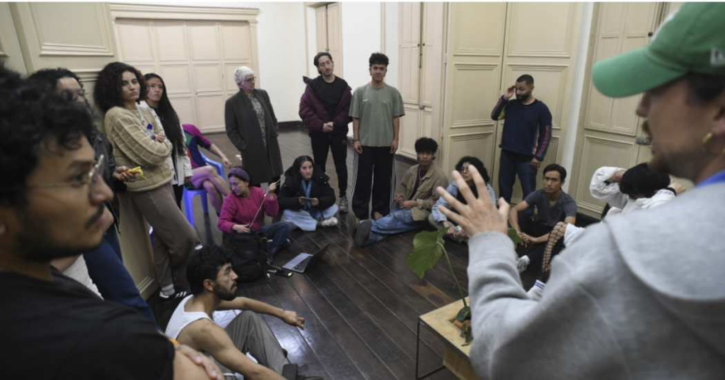 Imagen de varios jóvenes en una aula escuchando a un hombre mayor que habla.