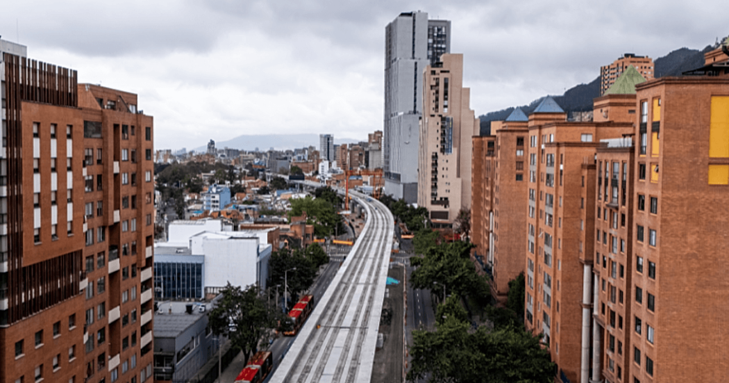 Vista de un tramo elevado de la Línea 1 del Metro de Bogotá en construcción, rodeado de edificios residenciales y de oficinas.