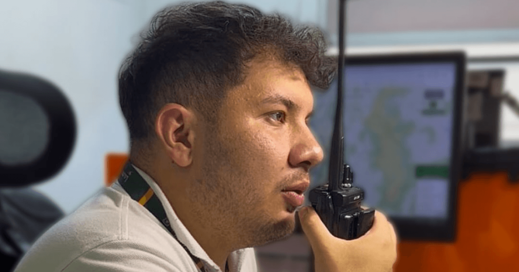 persona utilizando un radio portátil en centro de monitoreo de emergencias, con pantallas de información al fondo para el seguimiento de eventos en Bogotá.