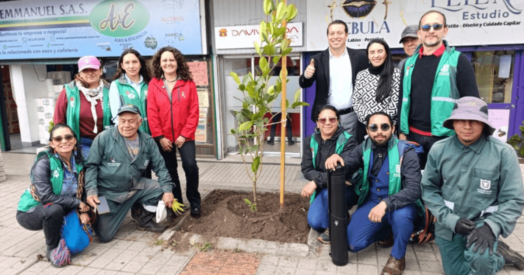 Grupo de personas del Jardín Botánico y del centro comercial Los Héroes posa alrededor de un árbol recién sembrado en un andén.