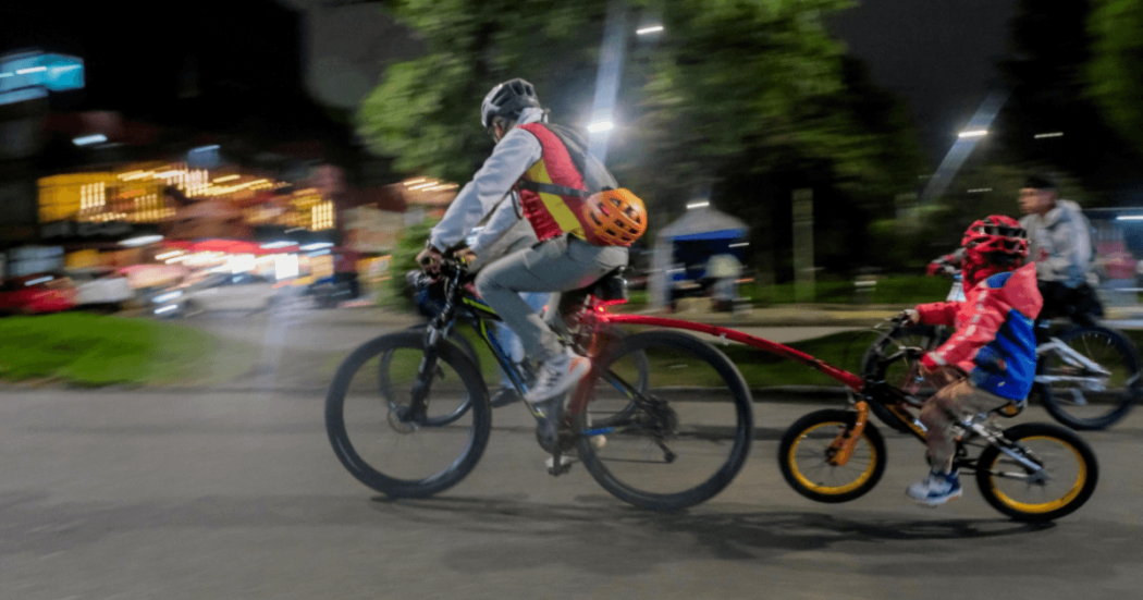 Persona adulta y menor de edad recorren una vía en bicicleta durante una jornada nocturna en Bogotá.