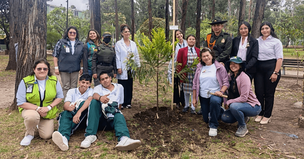 Grupo de personas participa en una jornada de siembra de árboles y arbustos en el Bosque Urbano San Carlos, junto a ejemplares recién plantados y rodeados de vegetación y árboles.