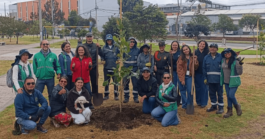 Grupo de personas posa alrededor de un árbol recién sembrado durante una jornada de siembra y restauración ecológica en Bogotá.