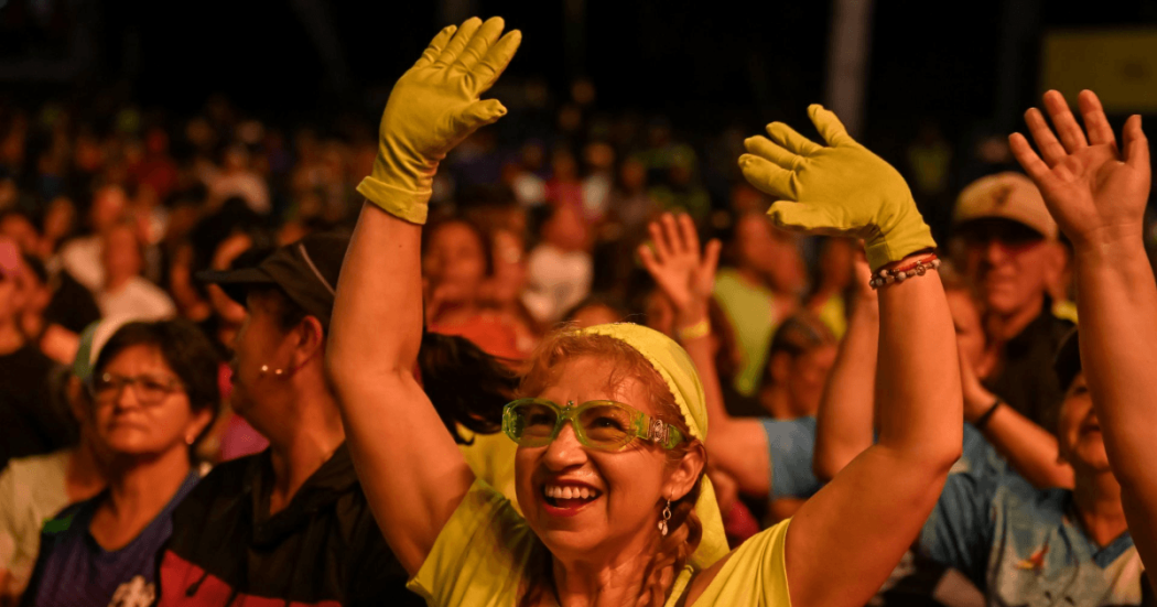 Persona con guantes y gafas de color verde levanta los brazos entre el público durante un evento nocturno al aire libre en Bogotá.