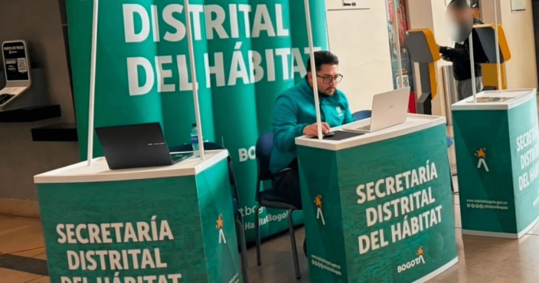 Foto que muestra un señor con un computador y avisos con el texto Secretaría Distrital del Hábitat