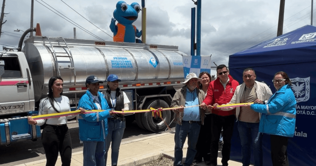 Foto que muestra un grupo de personas sonriendo sosteniendo una cinta y un carrotanque en el fondo