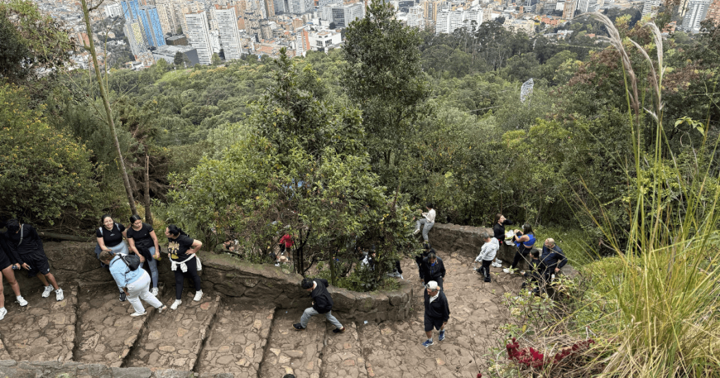Foto de personas ascienden los escalones del sendero de Monserrate en un día despejado y con vista panorámica de Bogotá.