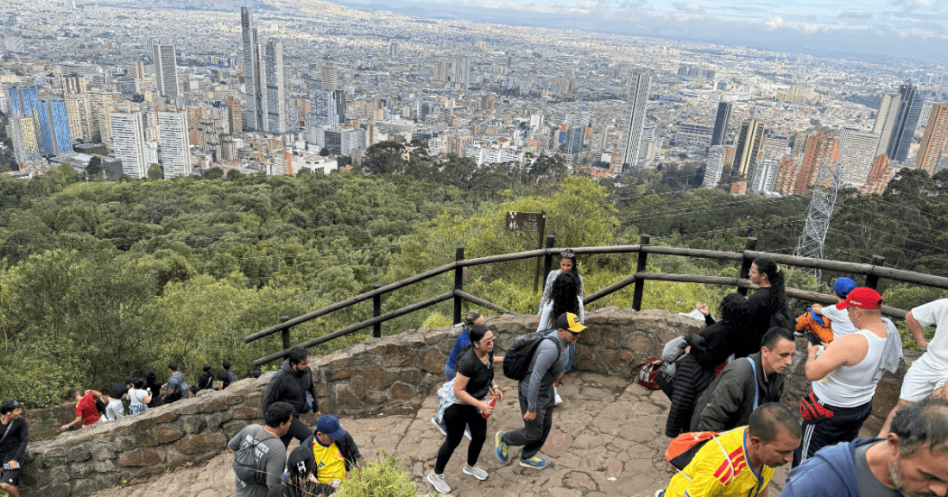 Personas acienden por el sendero de Monserrate con un fondo panorámico de la ciudad de Bogotá donde se observan edificios y zonas residenciales