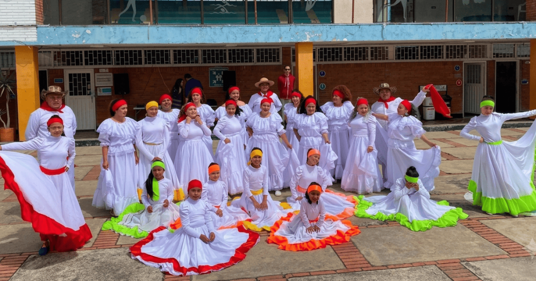 Grupo de personas con trajes folclóricos blancos y detalles de colores durante presentación artística en patio escolar de Bogotá.