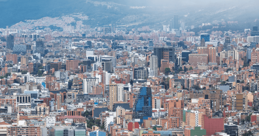Vista panorámica de Bogotá con edificios residenciales, vías principales, zonas comerciales y amplias áreas urbanas bajo un cielo nublado.
