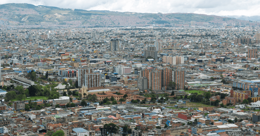Vista panorámica de Bogotá con edificios, zonas industriales y cerros bajo cielo nublado.