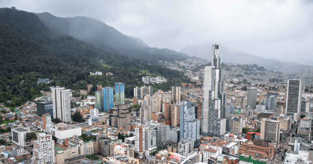 Vista panorámica de Bogotá con edificios residenciales y comerciales de diferentes alturas en primer plano, y los Cerros Orientales en un día nublado.