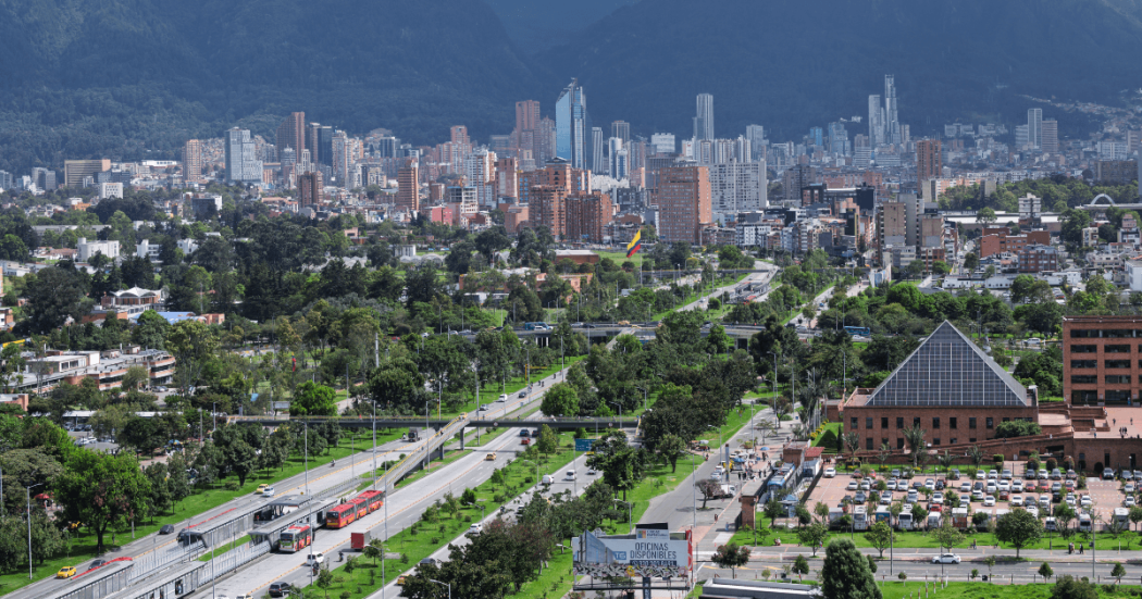 Vista panorámica de Bogotá con corredores viales, amplias zonas verdes, edificaciones residenciales y comerciales, y cerros orientales al fondo.