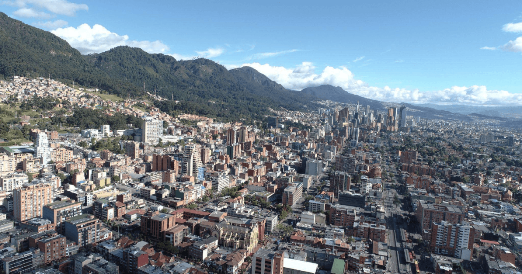 Vista panorámica de Bogotá con edificaciones, corredores viales y cerros orientales bajo cielo despejado.