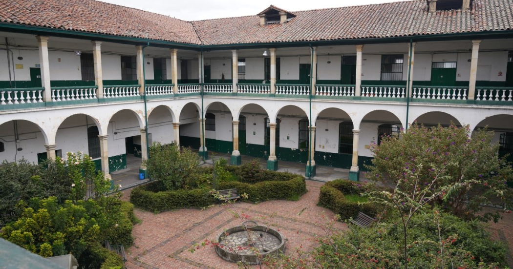 Foto que muestra un edificio de dos pisos con paredes blancas y verdes y un jardín en la mitad 