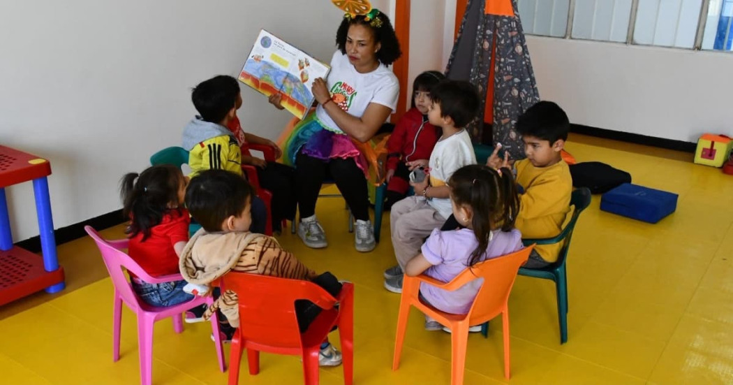 Niños en mesa redonda leyendo un libro con una profesora