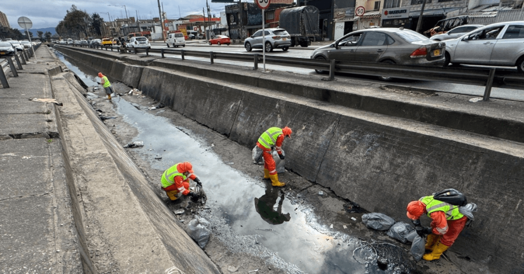 Foto que muestra dos personas con el uniforme de Aguas Bogotá limpiando un canal de agua 