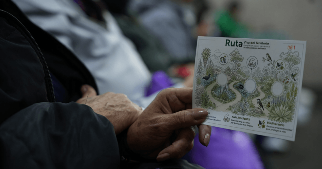 Persona sostiene una tarjeta ilustrada de la Ruta Viva del Territorio con flora, fauna y estaciones ambientales.