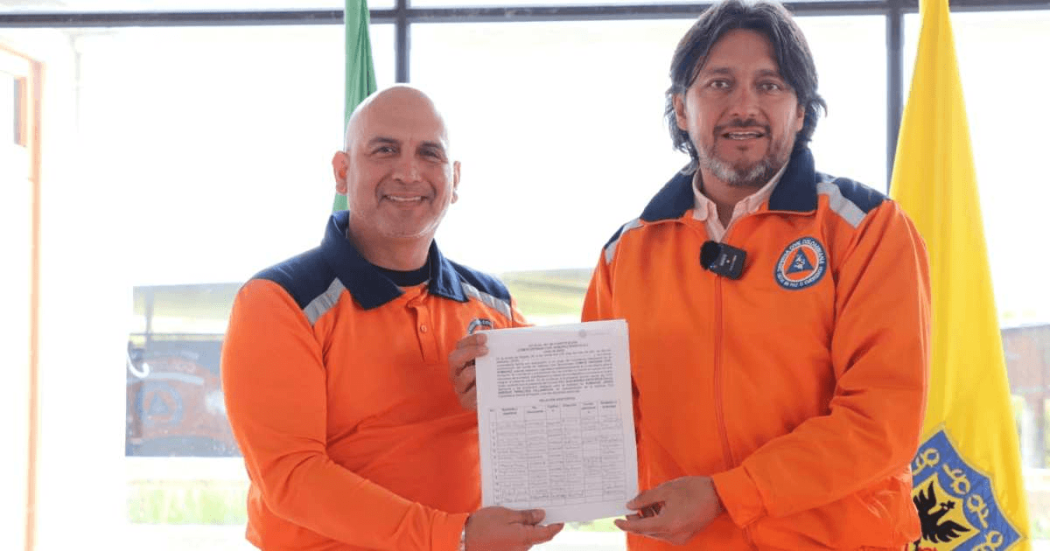 Foto que muestra dos personas sonriendo con un documento en la mano