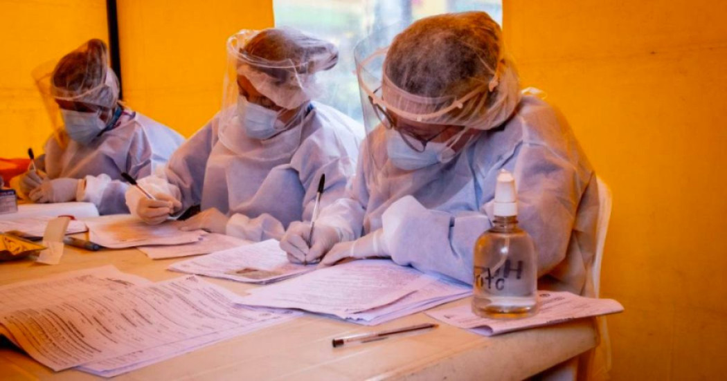 Foto que muestra dos personas con gorro y guantes de enfermería escribiendo en un papel