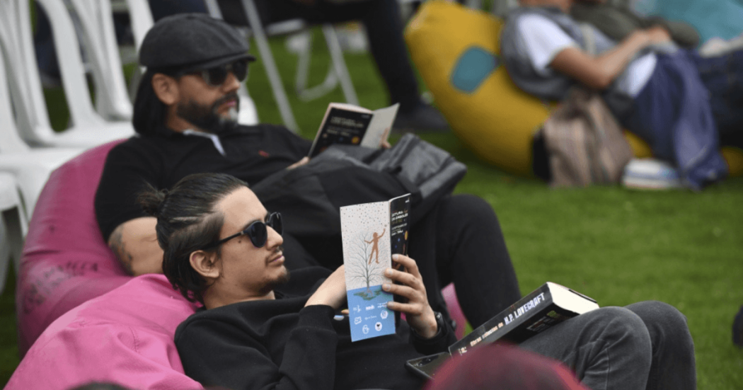 Imagen de hombres sentados en sillones al aire libre con libros abiertos.