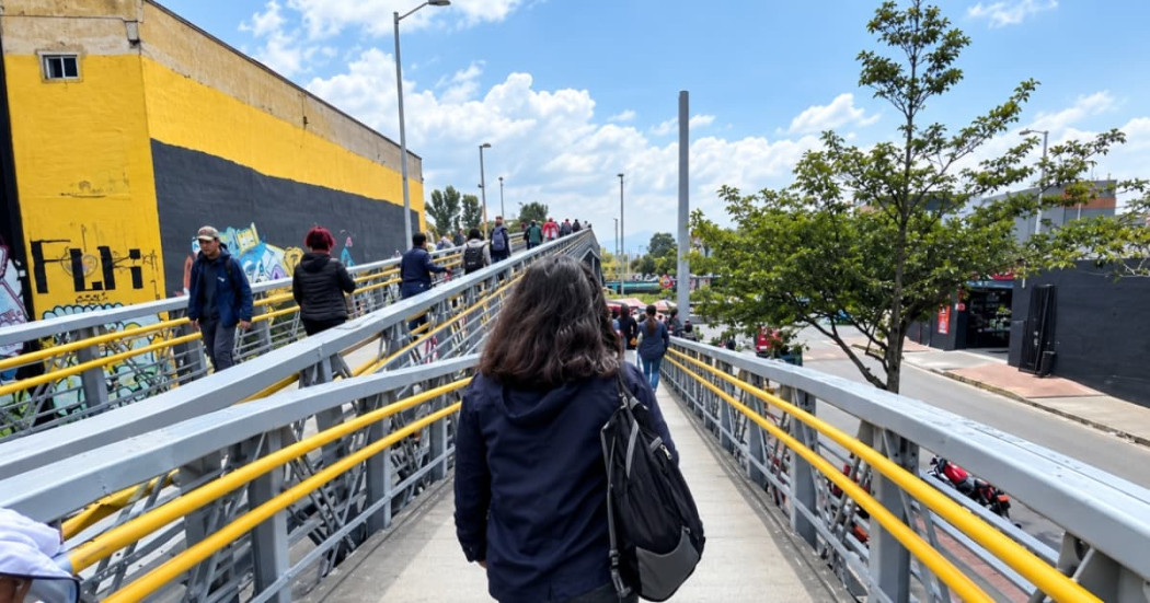 Foto de hombres y mujeres caminando por un puente peatonal en Bogotá.
