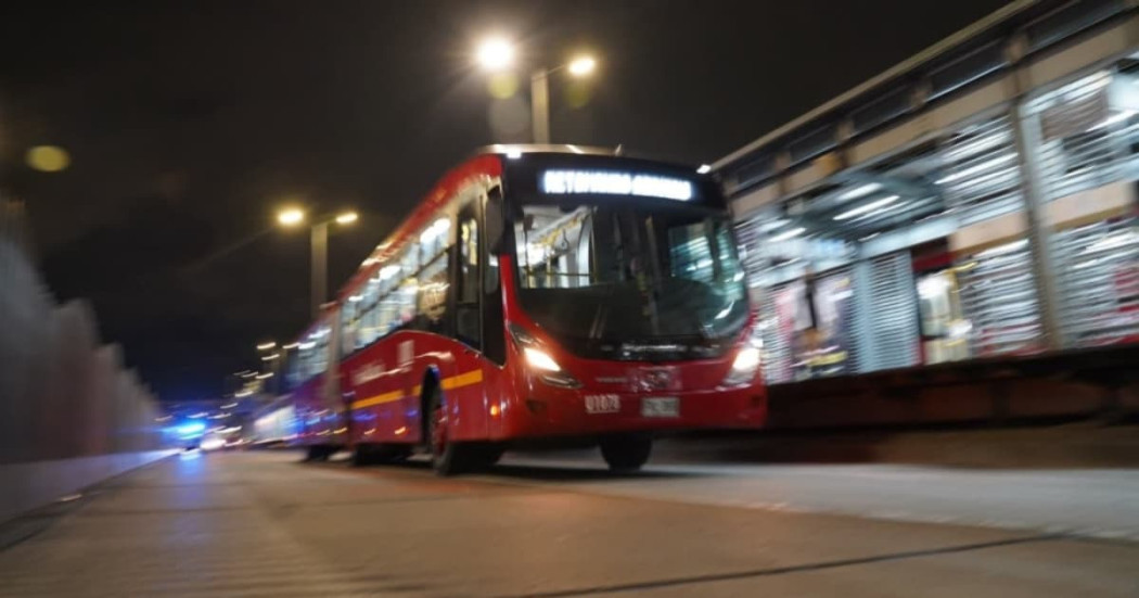 Foto de una estación y un bus de TransMilenio con iluminación de alumbrado público en Bogotá.