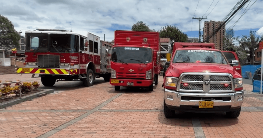 Vehículos del Cuerpo Oficial de Bomberos de Bogotá, entre ellos una máquina extintora, un camión de apoyo y una camioneta de emergencia, estacionados sobre una plazoleta de ladrillo.
