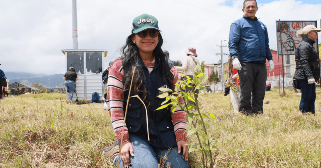 Persona participante de una actividad ambiental sostiene una plántula junto a vegetación nativa en un humedal de Bogotá, durante una jornada de formación y conservación ambiental.