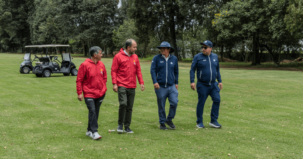 Cuatro personas caminan sobre el césped del campo de golf del Parque La Florida. Dos visten chaquetas rojas y dos chaquetas azules.