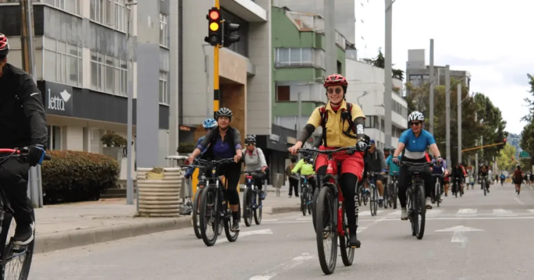 Grupo de personas en bicicleta recorre una vía urbana durante una jornada de Ciclovía. En primer plano se observa una persona con casco y chaleco reflectivo, mientras detrás avanzan más ciclistas por una avenida rodeada de edificios y señalización vial.