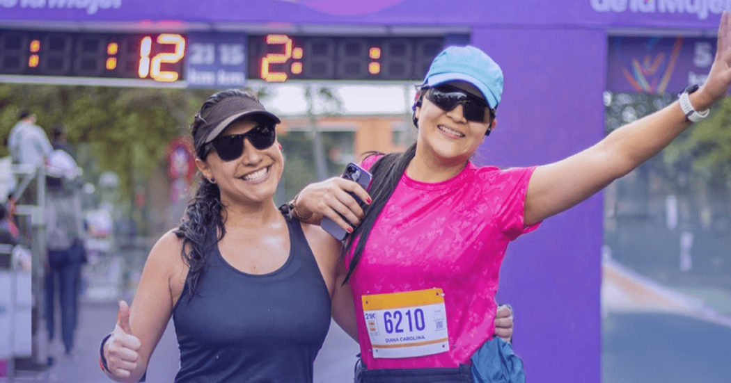 Dos participantes de la Carrera de la Mujer posan frente al arco de meta con números de competencia visibles