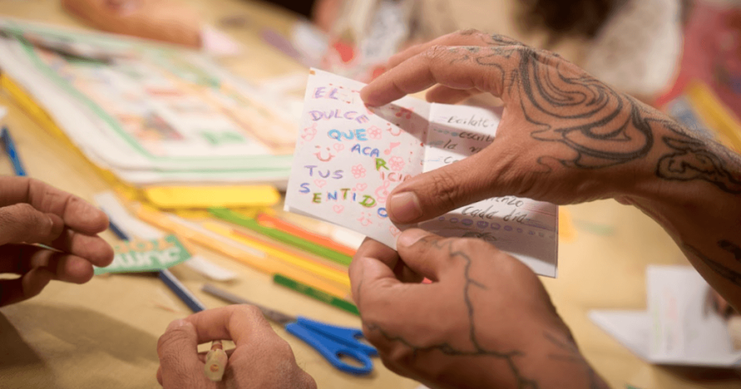 Imagen de manos con tatuajes con libro en hojas pequeño en una biblioteca de Bogotá.
