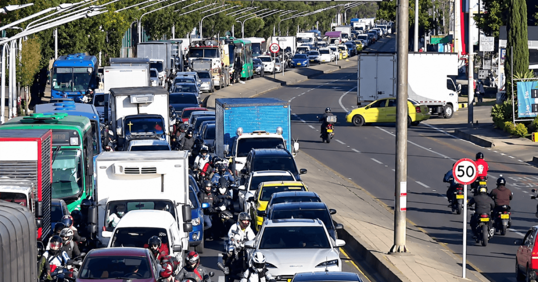 Vista elevada de una avenida urbana con tráfico vehicular intenso y congestionado, donde circulan buses, camiones, automóviles, taxis y motocicletas en Bogotá.