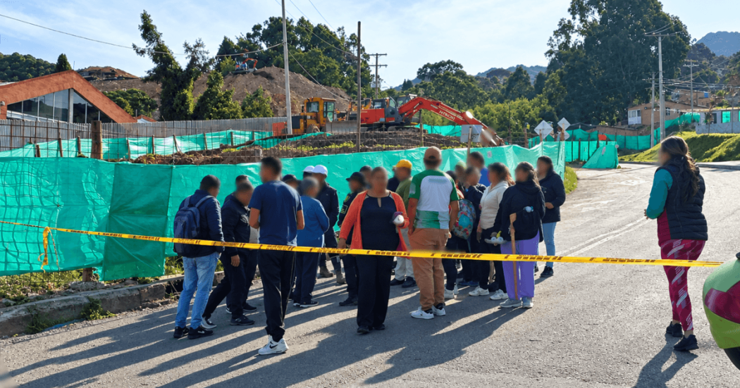 Personas reunidas en una vía observan una situación de movilidad delimitada con cinta amarilla. En el lugar se ven vehículos detenidos, carpas blancas y banderines de colores.