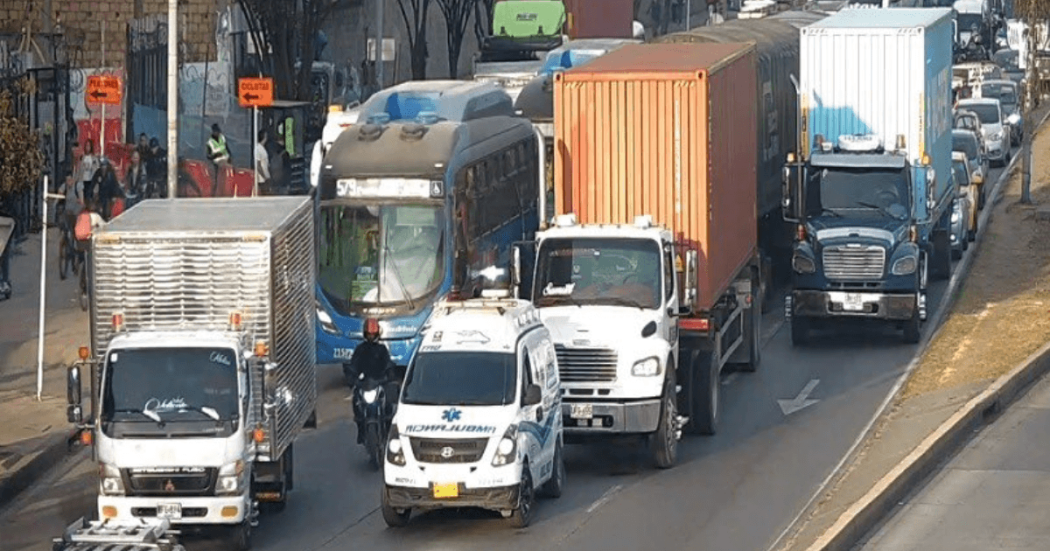 Vehículos particulares, camiones de carga y un bus circulan lentamente en una vía congestionada de Bogotá, con varios carriles ocupados por tráfico denso.