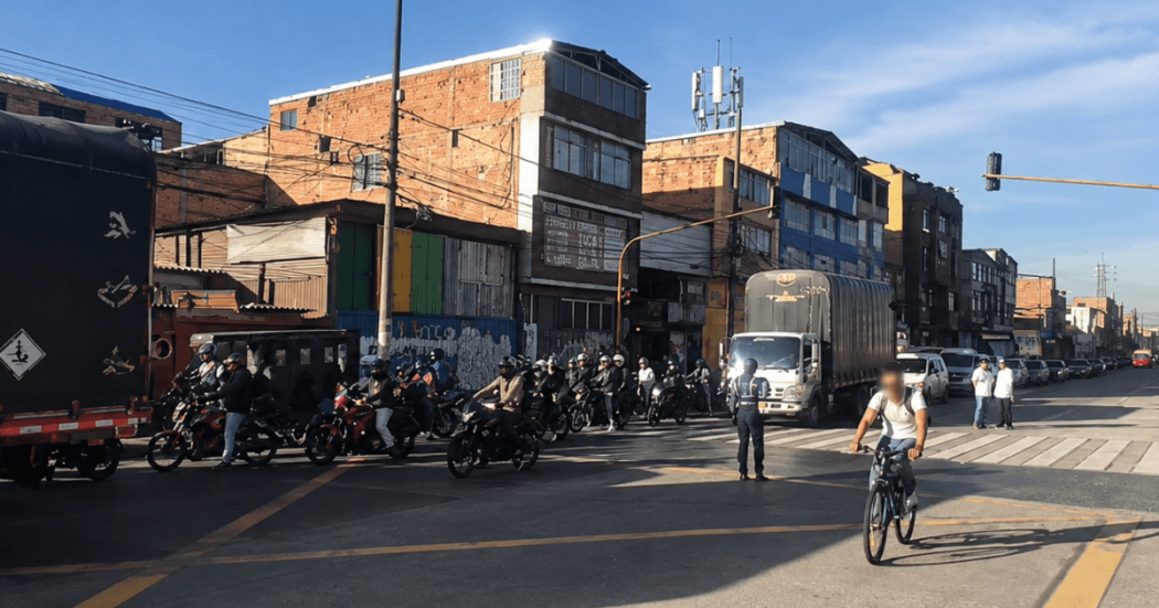 Intersección vial en Bogotá con alto flujo de motocicletas, camiones, vehículos particulares y un ciclista cruzando la vía.