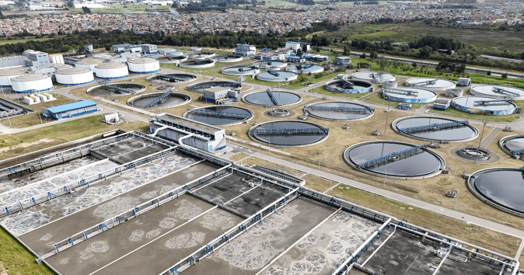 Vista aérea de la PTAR Salitre con múltiples tanques circulares y rectangulares para el tratamiento de aguas residuales, rodeados de estructuras operativas y canales.