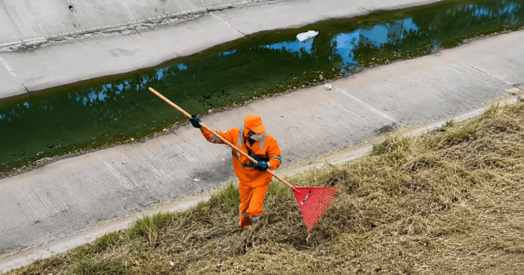 Foto que muestra una persona con el uniforme de Aguas Bogotá limpiando un canal de agua 